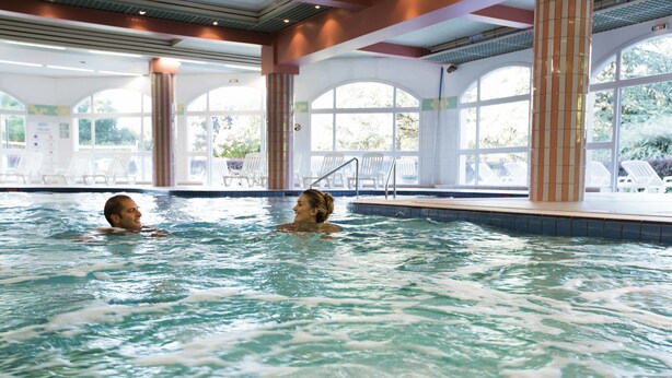 An indoor swimming pool with clear water, surrounded by lounge chairs and large windows. - Hotel & Spa Vacances Bleues Villa Marlioz (Aix-les-Bains)