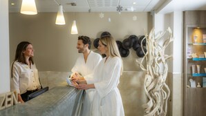 A spa reception area with a reception desk, a wall-mounted art piece, and a wooden cabinet with items on display. - Hotel & Spa Vacances Bleues Villa Marlioz (Aix-les-Bains)