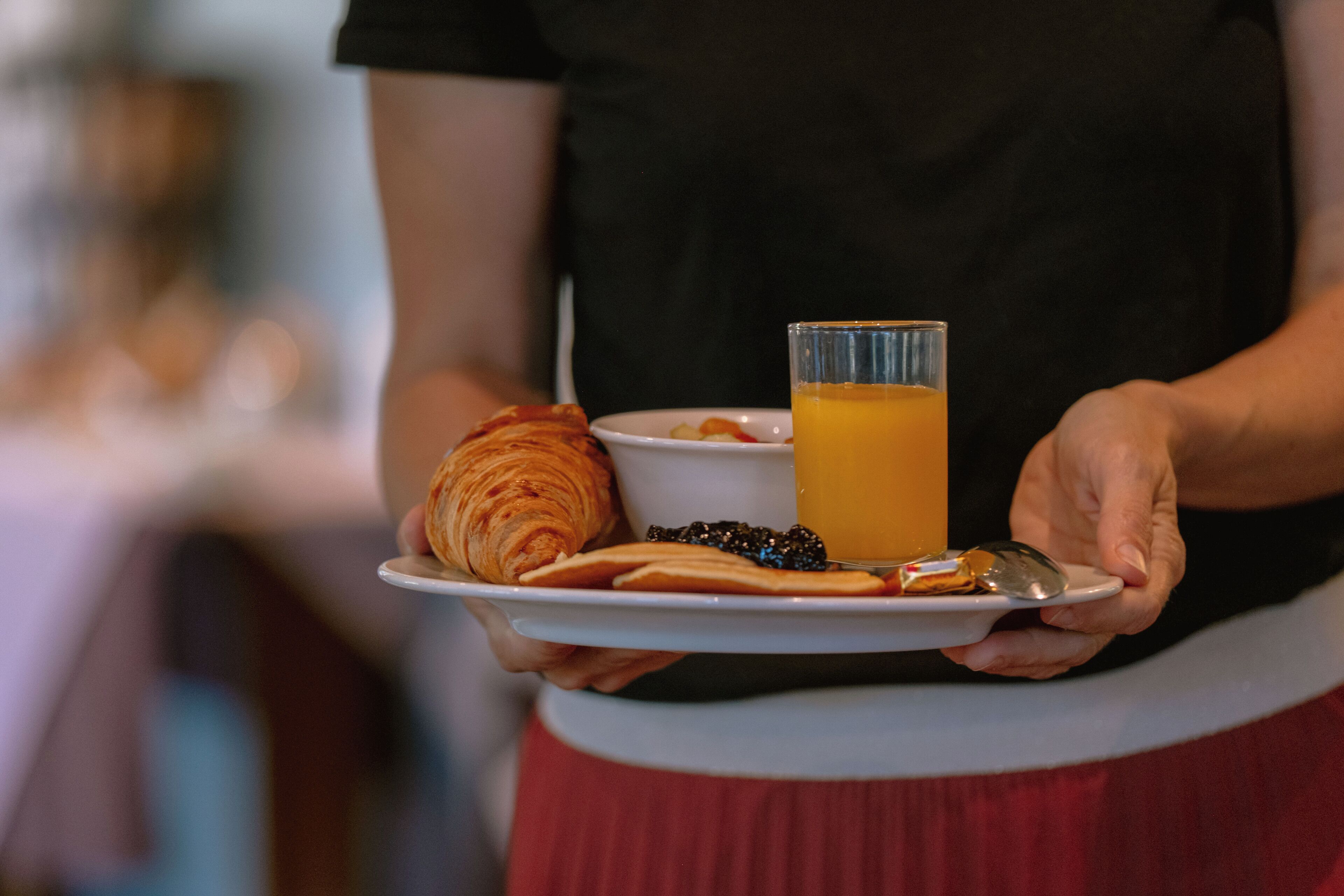 A person holding a plate with a croissant, a glass of orange juice, and a small bowl of berries.