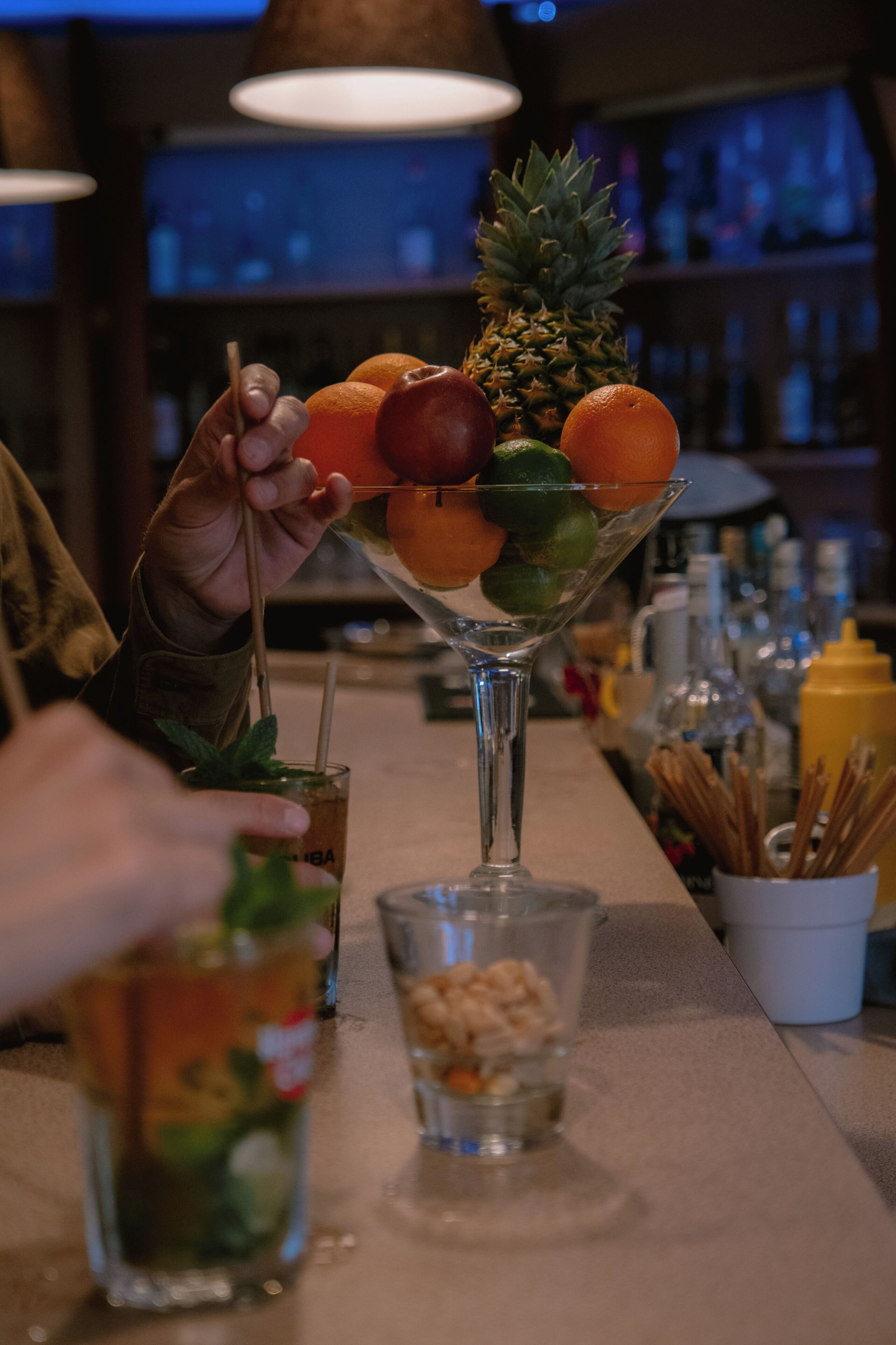 Un bar con una copa de martini que contiene fruta y una bebida con pajita.