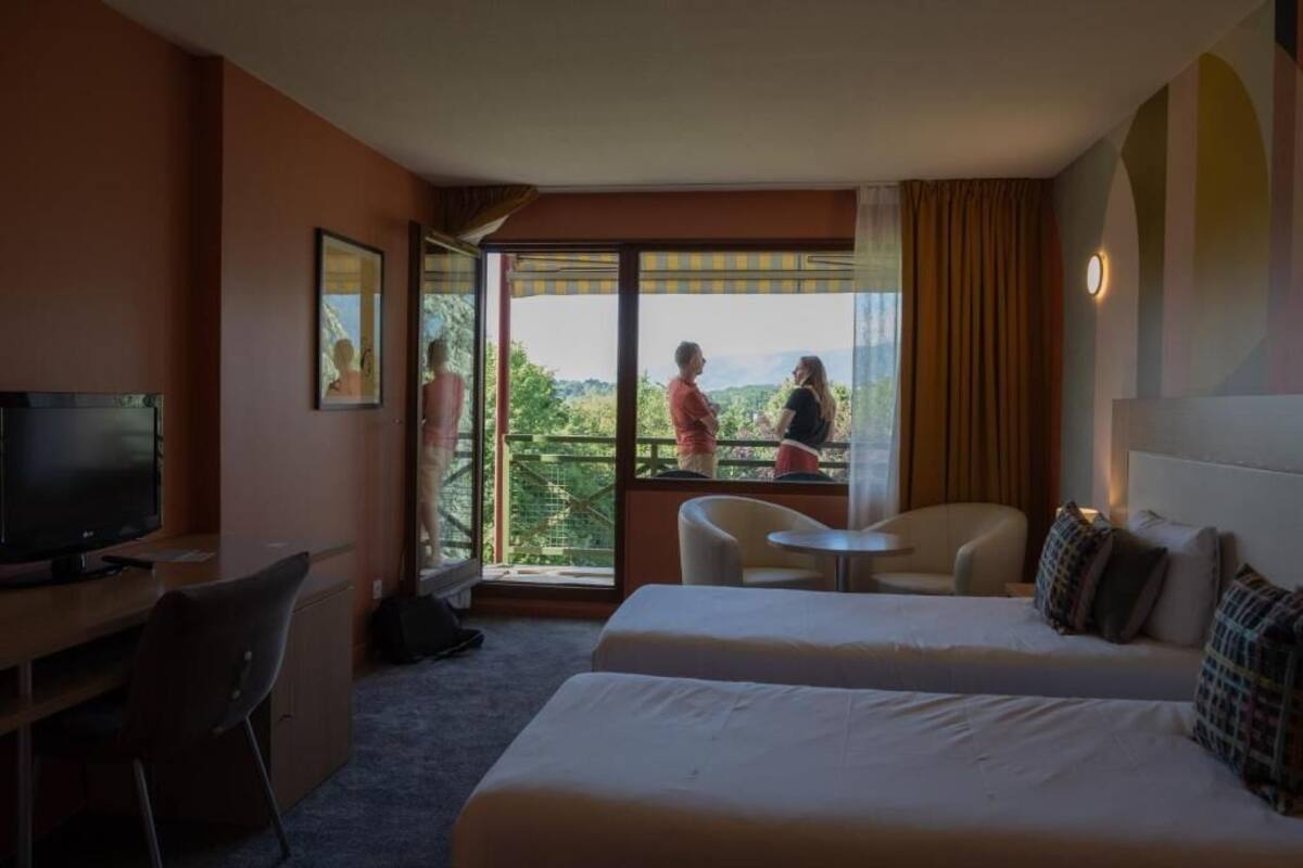 A hotel room with a bed, a desk, a TV, a balcony with a view, and a chair.