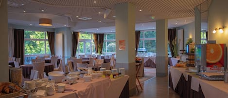 A spacious dining area with tables set for a buffet, large windows, and a ceiling with a unique pattern.