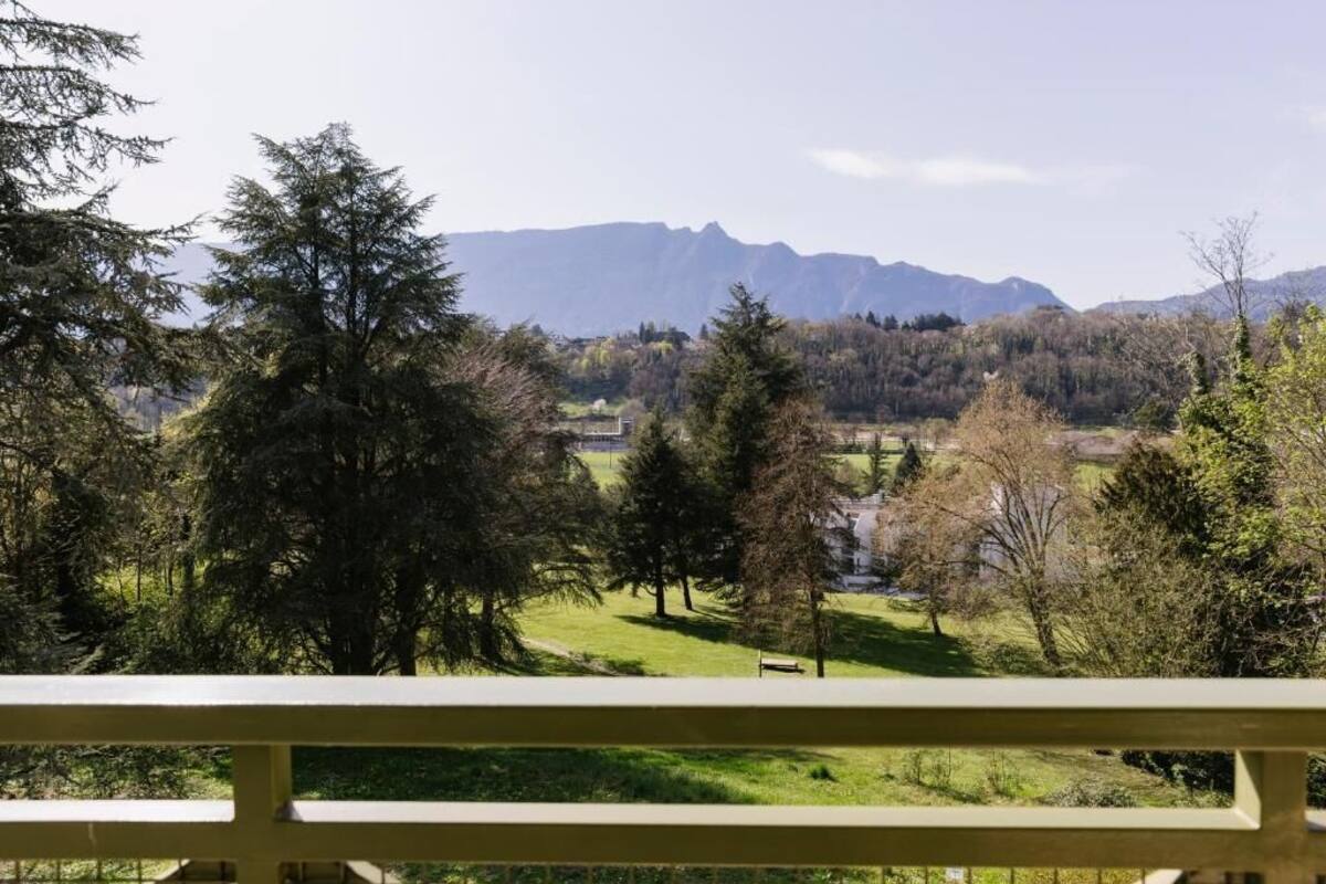 A view of a mountainous landscape with trees and a bench in the foreground.