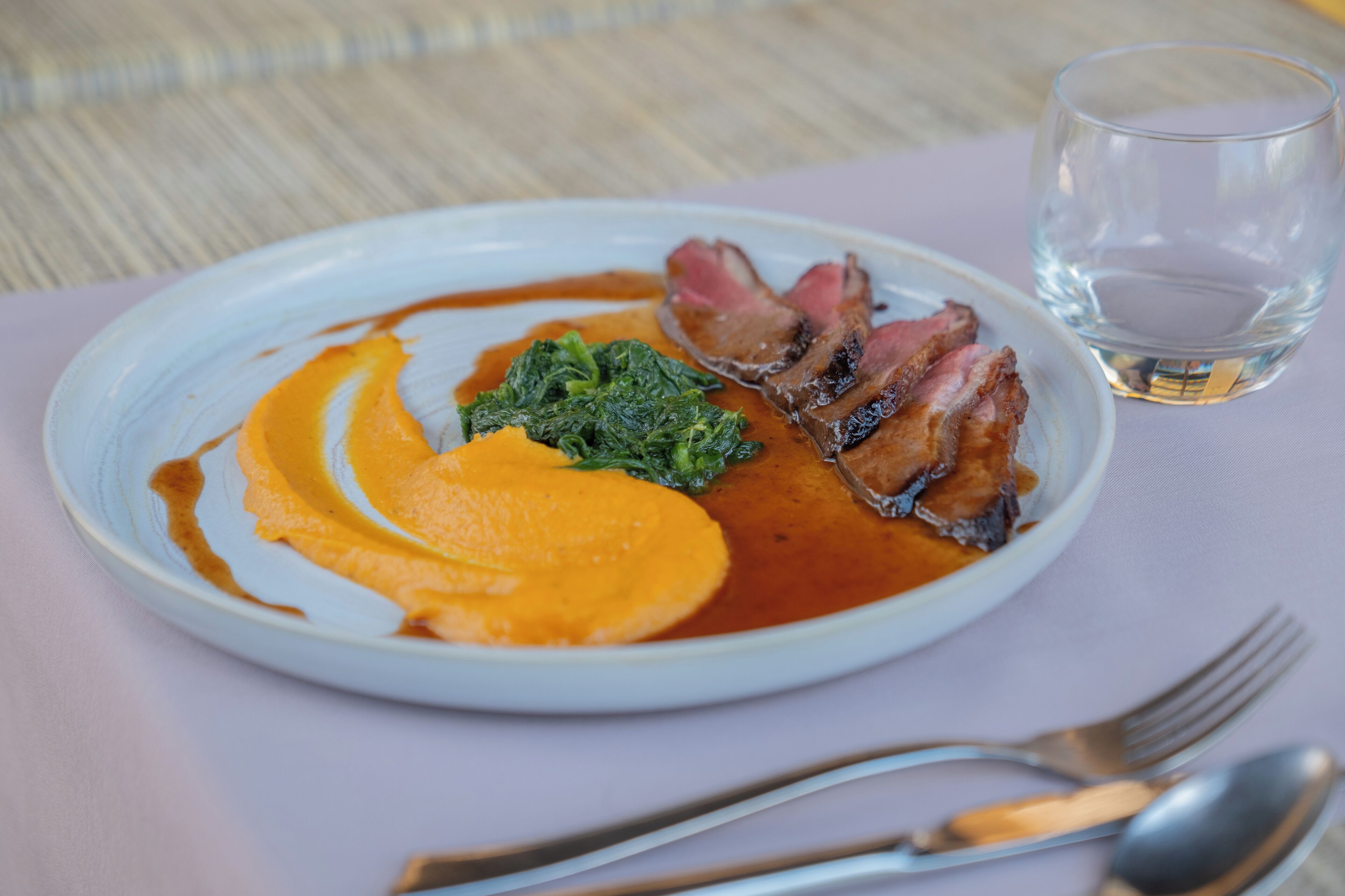 Un plato de comida con un vaso de agua y cubiertos sobre una mesa.