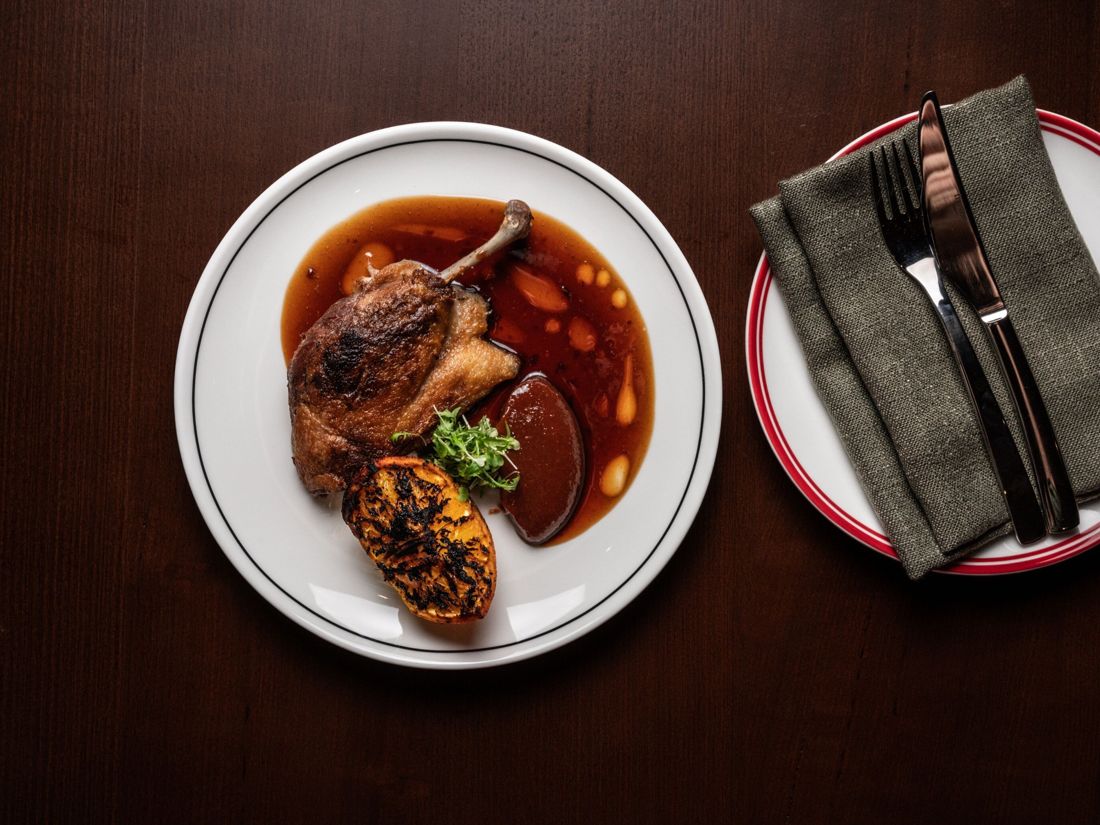 A plate with a grilled chicken leg, roasted potatoes, and a garnish on a wooden table.