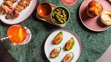 Una variedad de platos en una mesa, incluyendo brochetas, un bol de edamame y una fuente con sashimi de salmón.