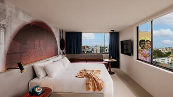 A hotel room with a large bed, a small table, a TV, and a city view.