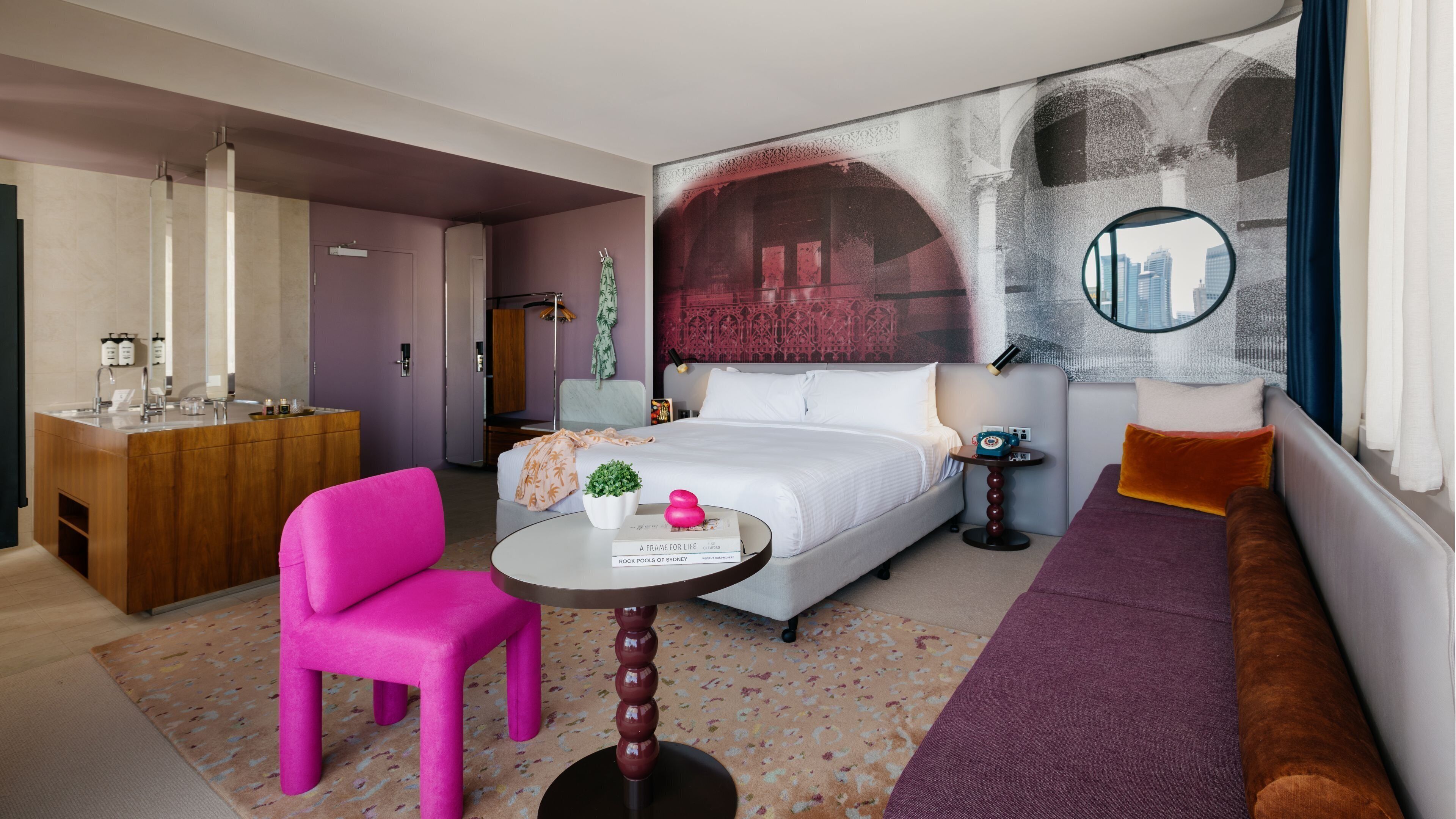A hotel room with a bed, a desk, a chair, a small table, a sofa, and a large artwork on the wall.