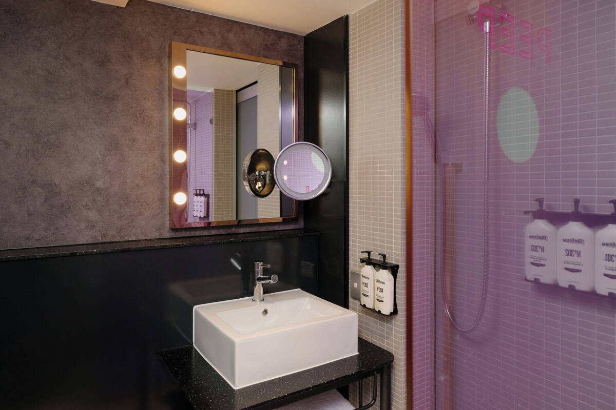 A bathroom with a large mirror, a sink, and a shower.