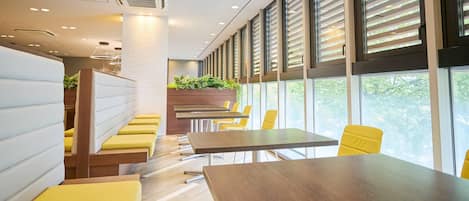 A modern meeting room with a long table, yellow chairs, and a seating area with cushioned benches.