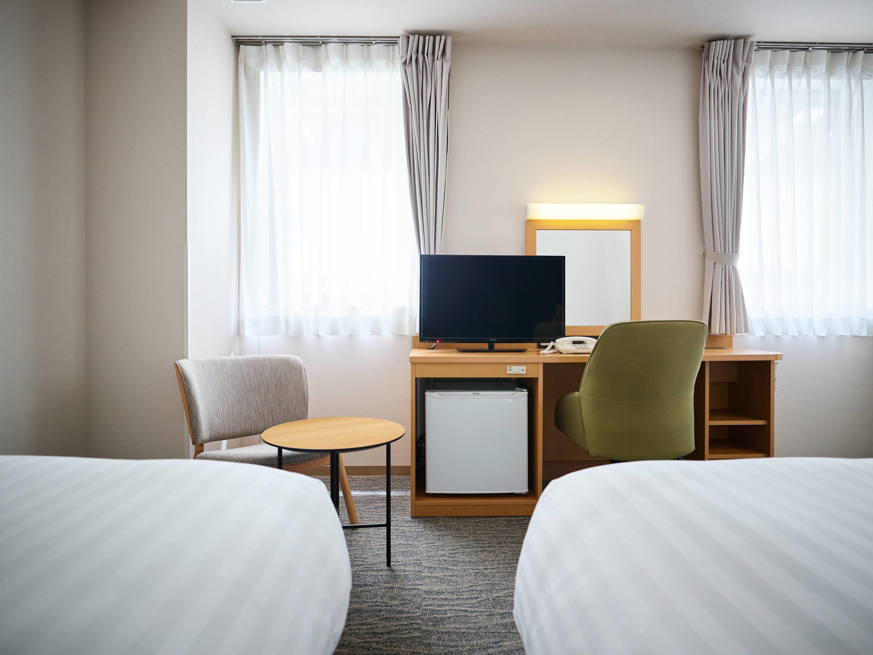 Habitación de hotel con dos camas, un escritorio con televisor, un refrigerador pequeño y dos sillas.