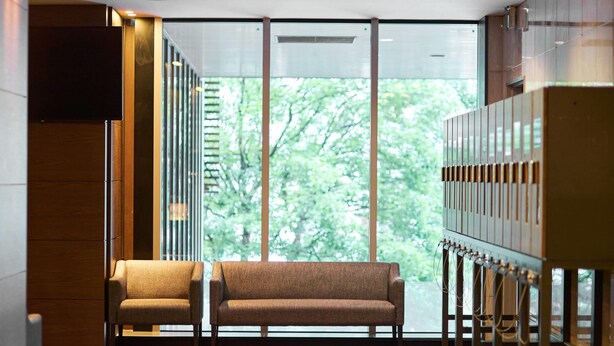 A modern interior with a sofa and chairs, a large window with a view of trees, and a wall-mounted cabinet. - Comfort Hotel Sendai West (Sendai)