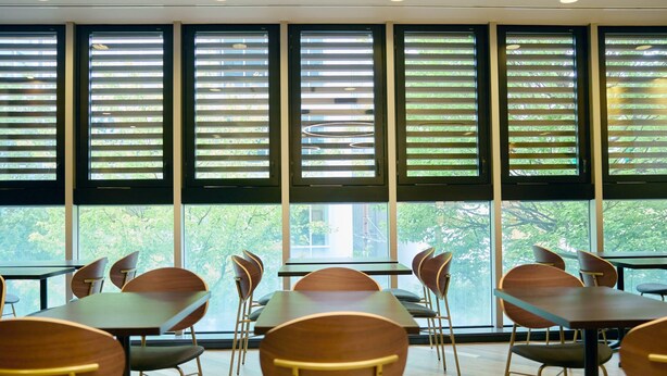 A modern interior with tables and chairs arranged for dining, large windows with blinds, and a view of greenery outside. - Comfort Hotel Sendai West (Sendai)
