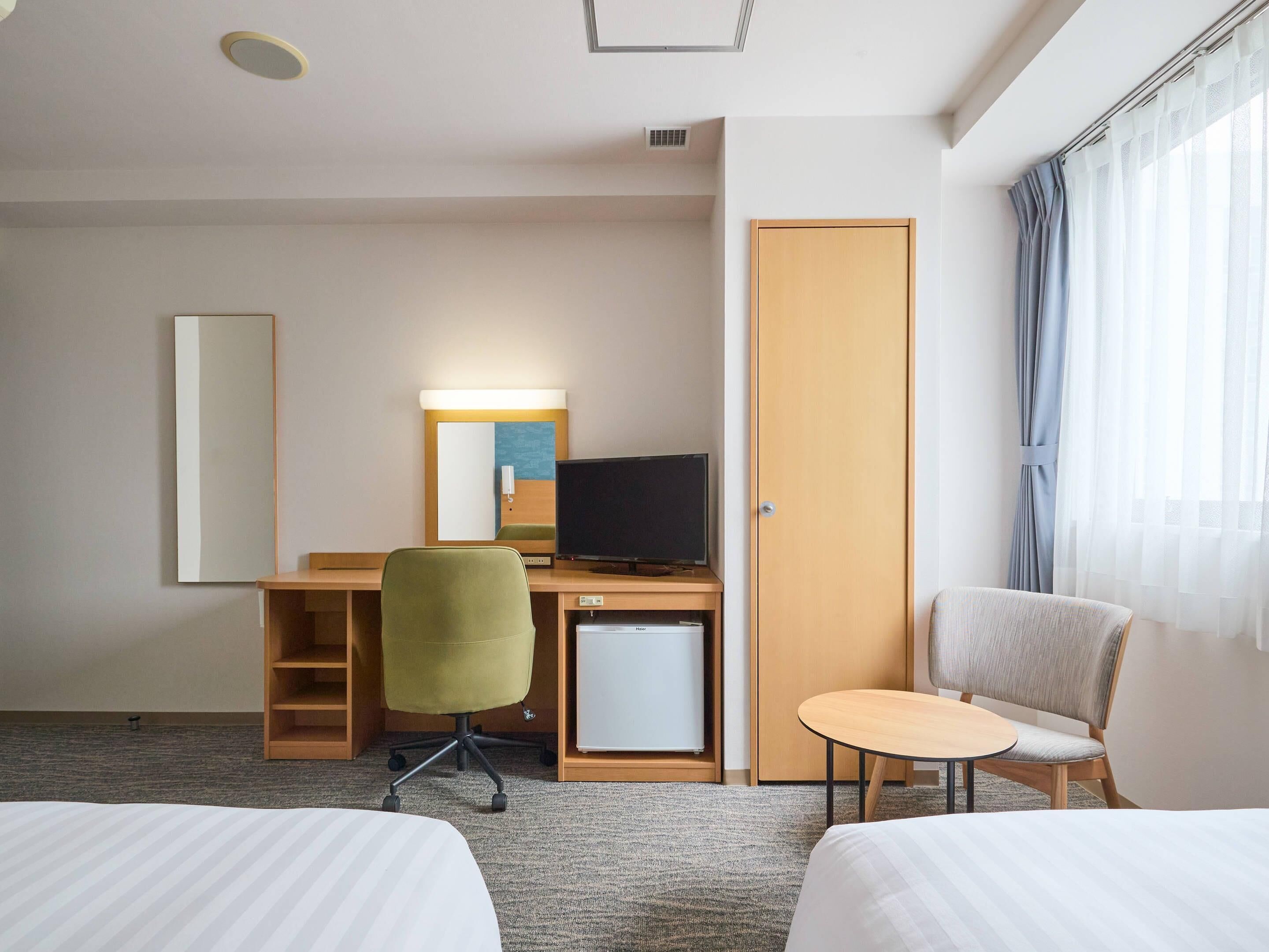 Hotellihuone, jossa on sänky, työpöytä tietokoneella, tuoli, pieni pöytä ja vaatekaappi.
