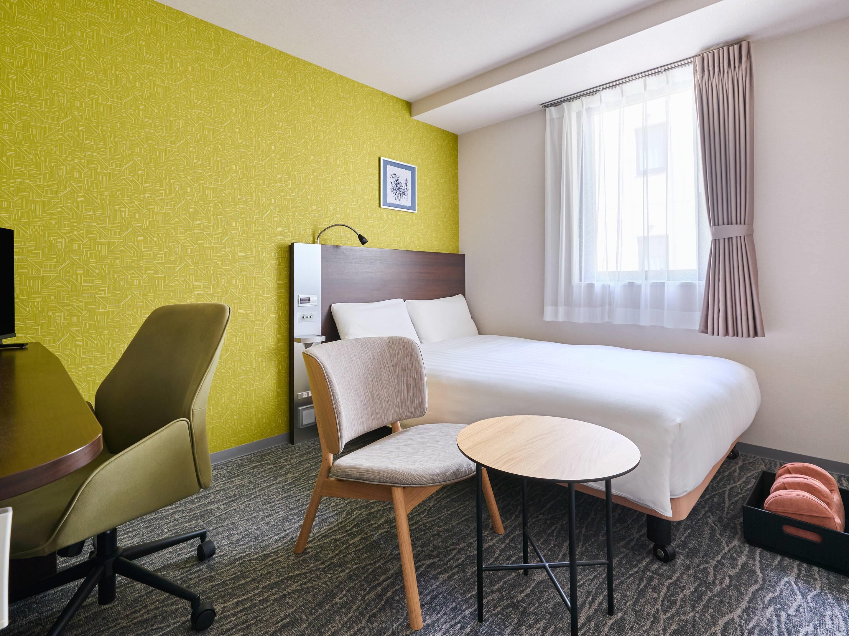 Una camera d'albergo con un letto, una scrivania, una sedia, un tavolino e una finestra con tende.