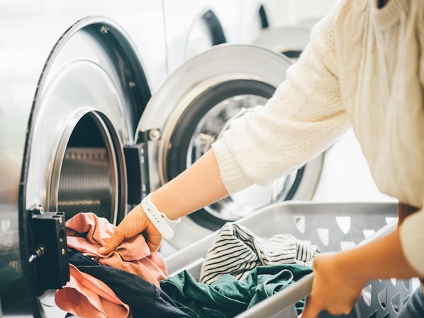 A person loading clothes into a front-loading washing machine.