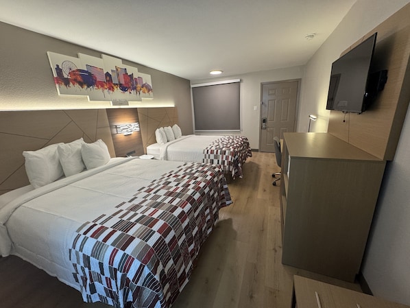 A hotel room with two beds, a TV mounted on the wall, a desk, and a painting of a city skyline.