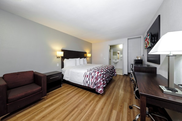 A hotel room with a bed, a desk, a chair, a TV, and a lamp.