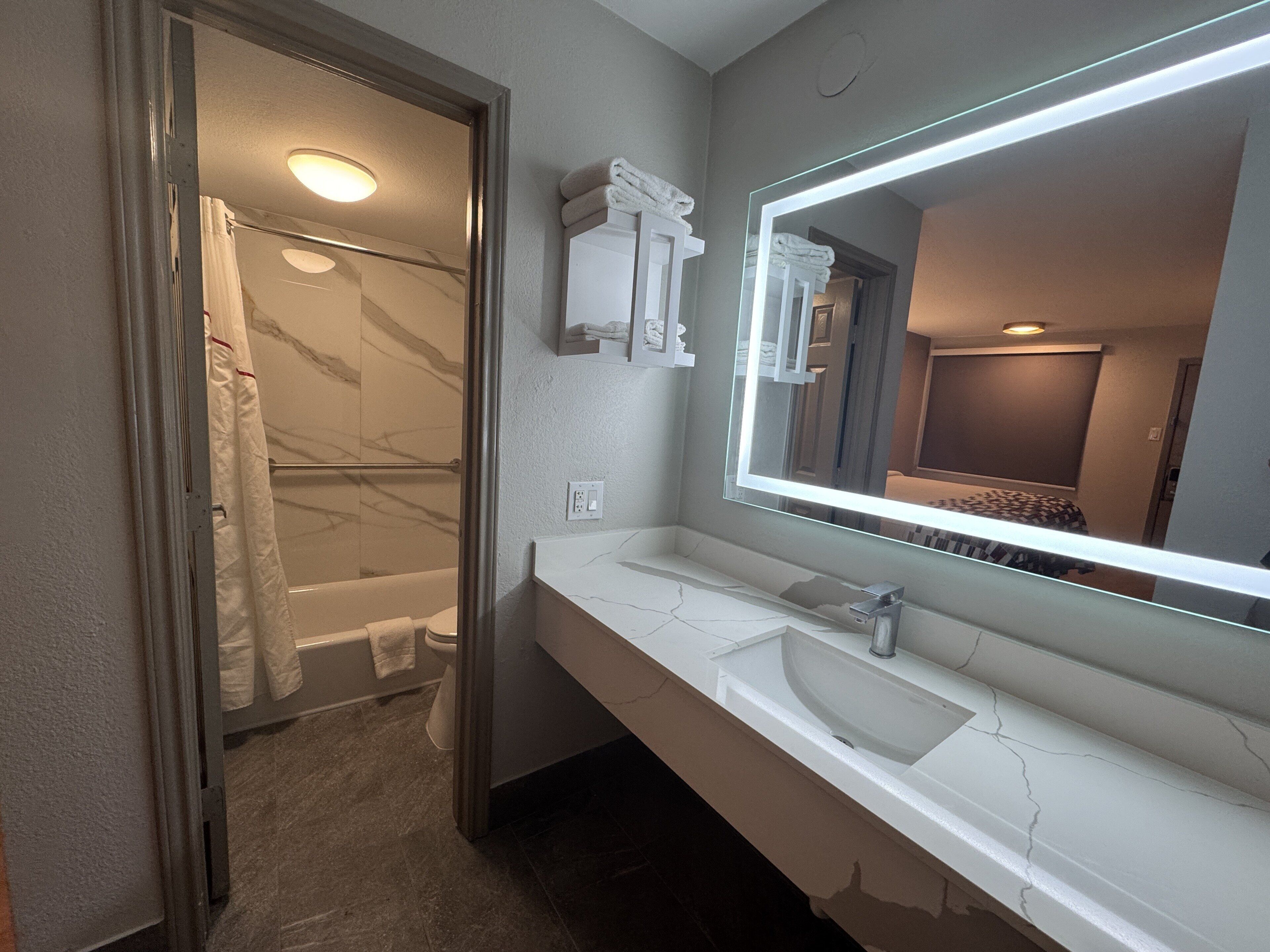 A modern bathroom with a glass shower enclosure, a white vanity with a large mirror, and a visible bathroom door.