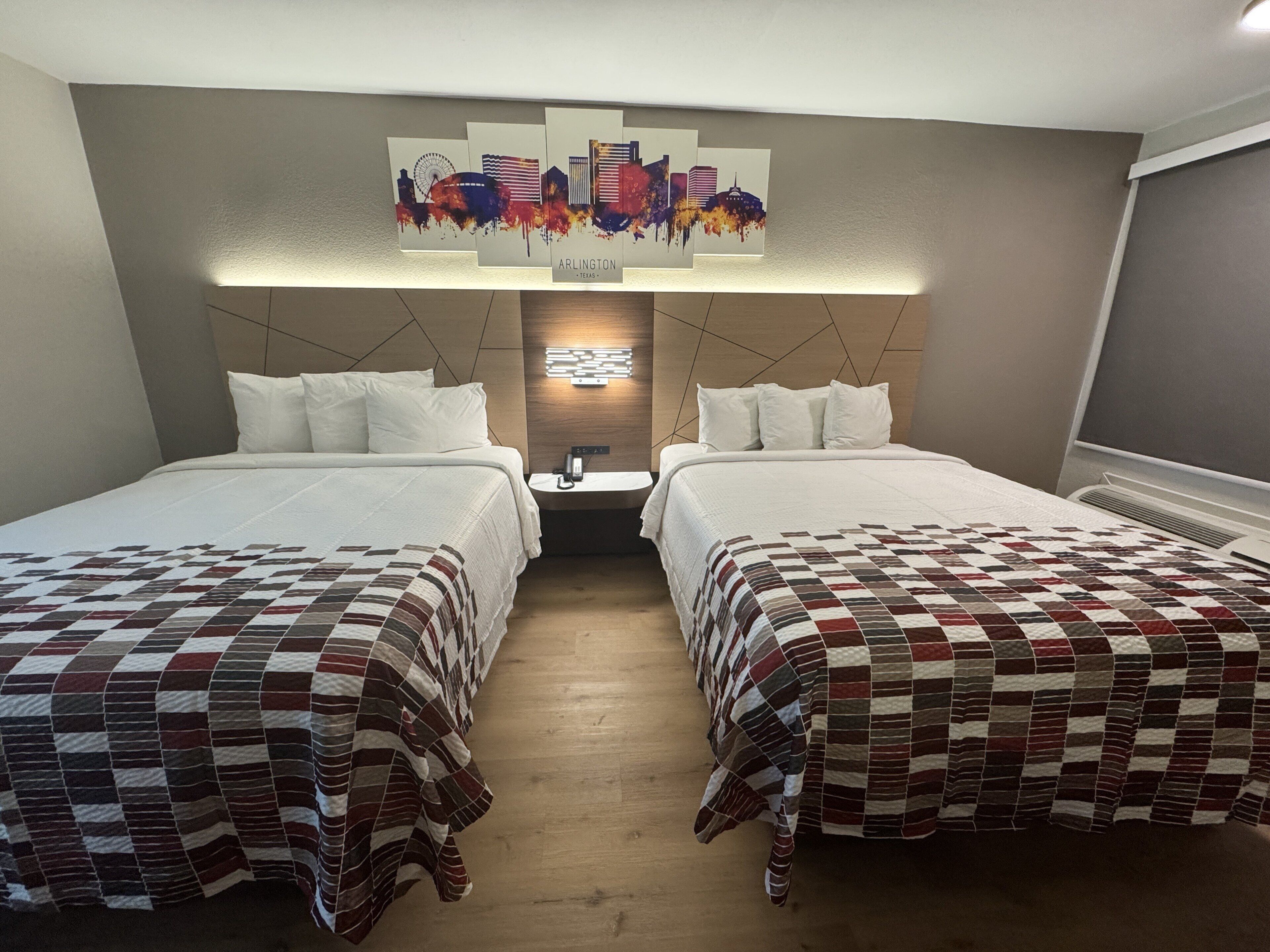A hotel room with two beds, a cityscape artwork on the wall, and a modern headboard design.