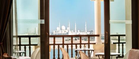 A balcony with a view of a white mosque, furnished with wicker chairs and a glass table.