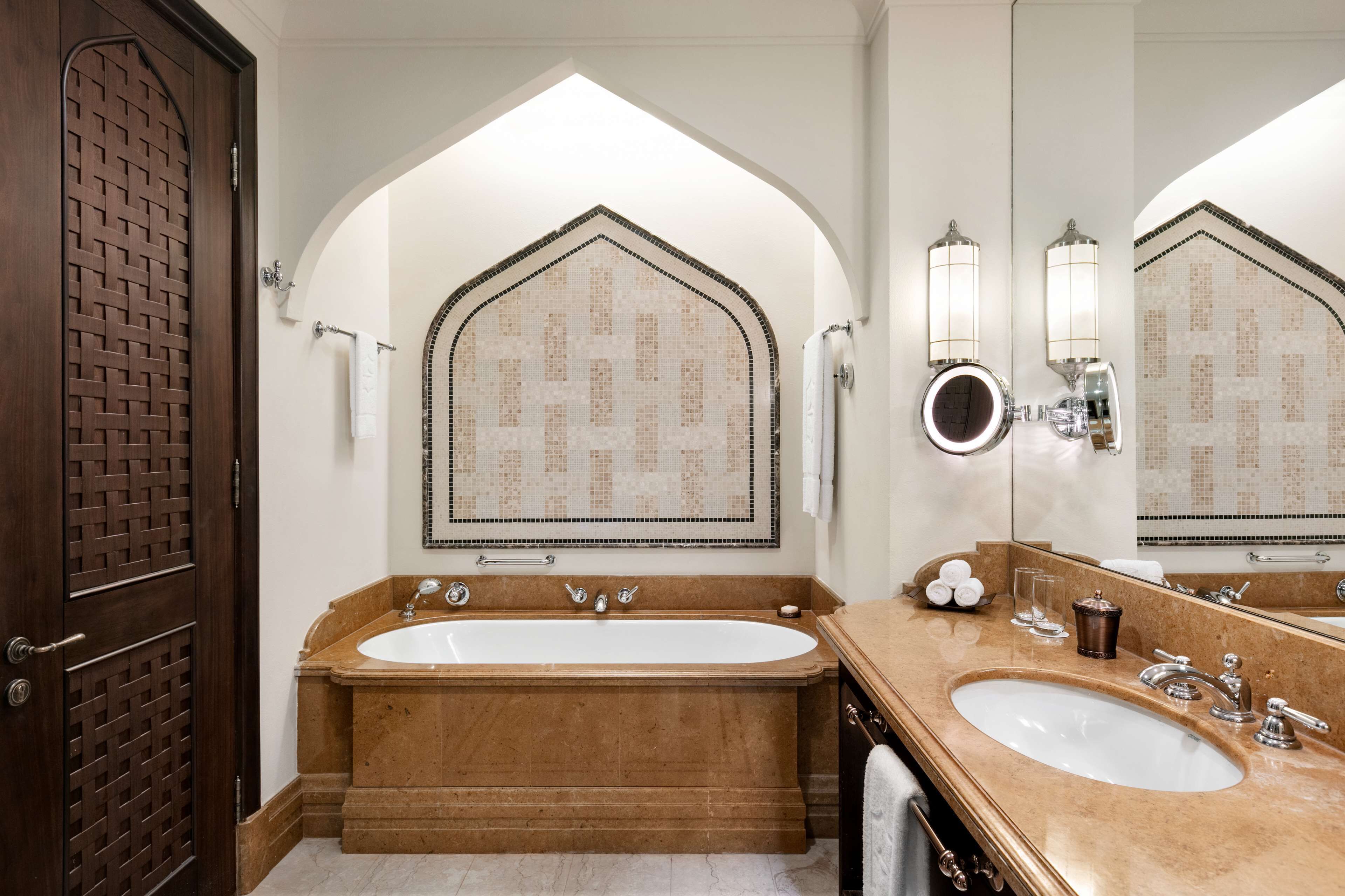 A bathroom with a large bathtub, a double sink, and a mirror with a decorative tile backsplash.