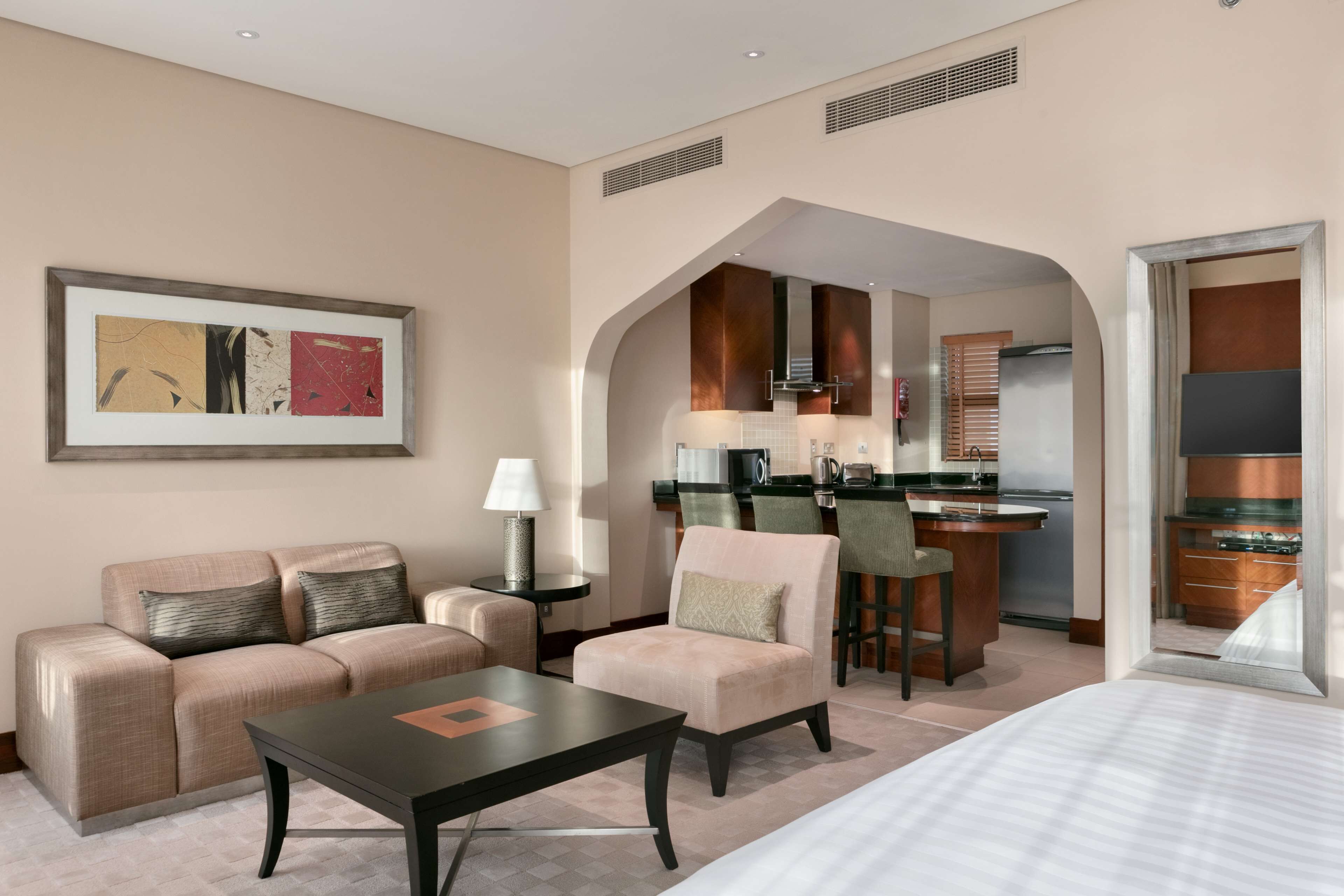 A hotel room with a sofa, armchair, dining table, and kitchenette.