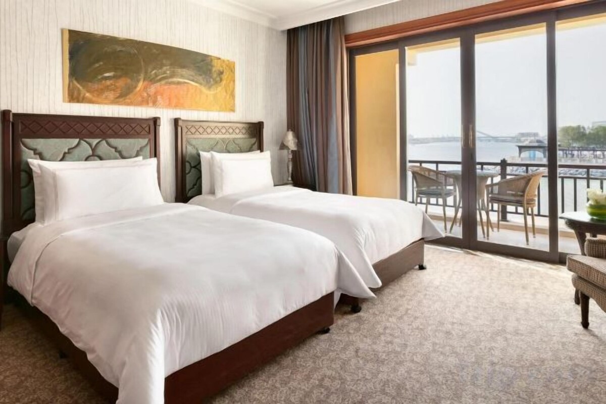 A hotel room with two beds, a large window, and a view of the water.