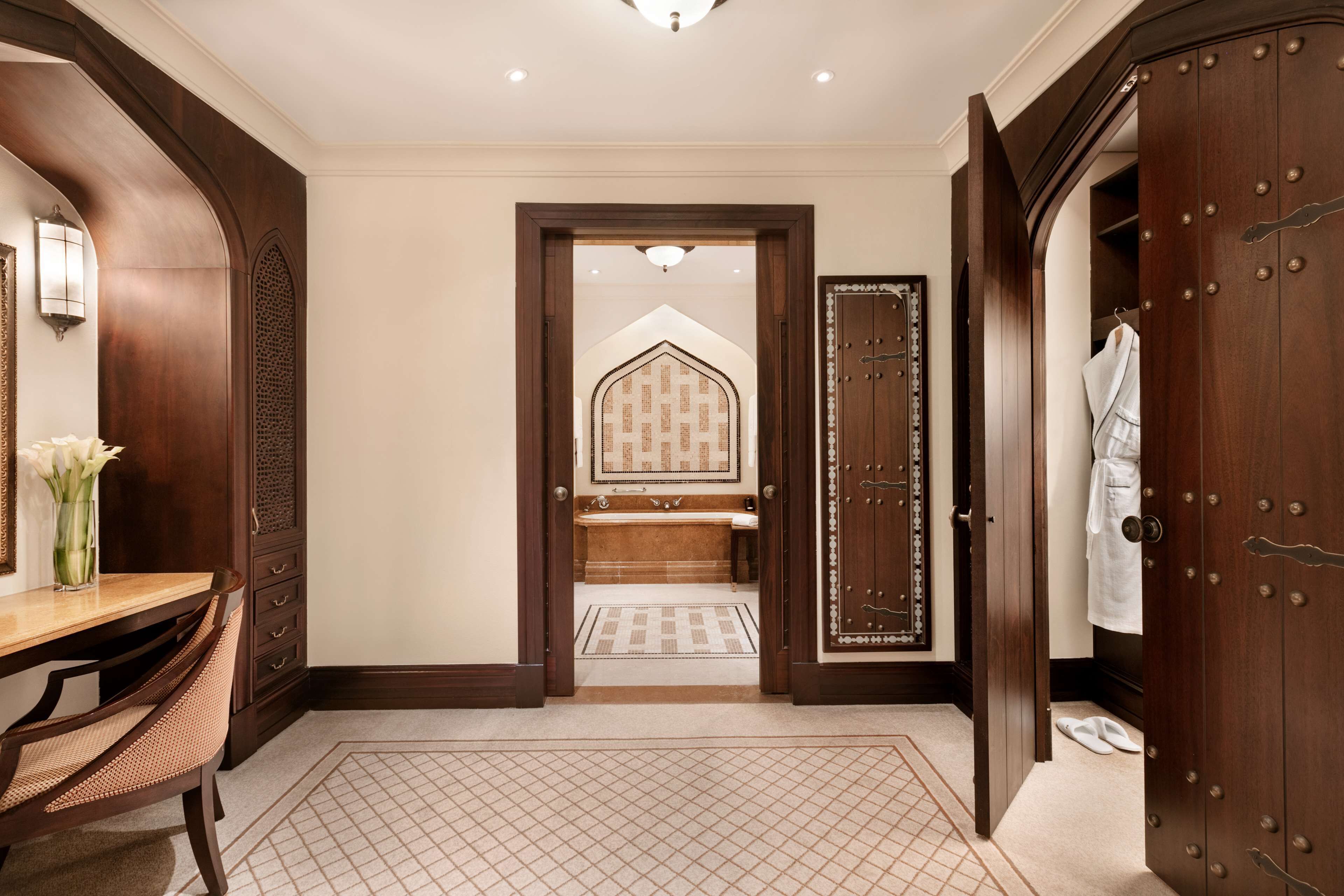 Une salle de bain spacieuse avec un grand miroir, un meuble-lavabo en bois et un dressing où est suspendu un peignoir.
