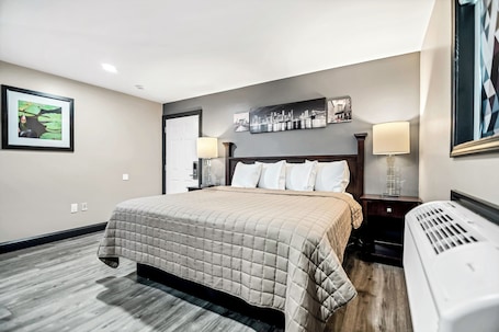 A hotel room with a bed, a nightstand, a lamp, a heater, and framed artwork on the walls.. Best Way Inn