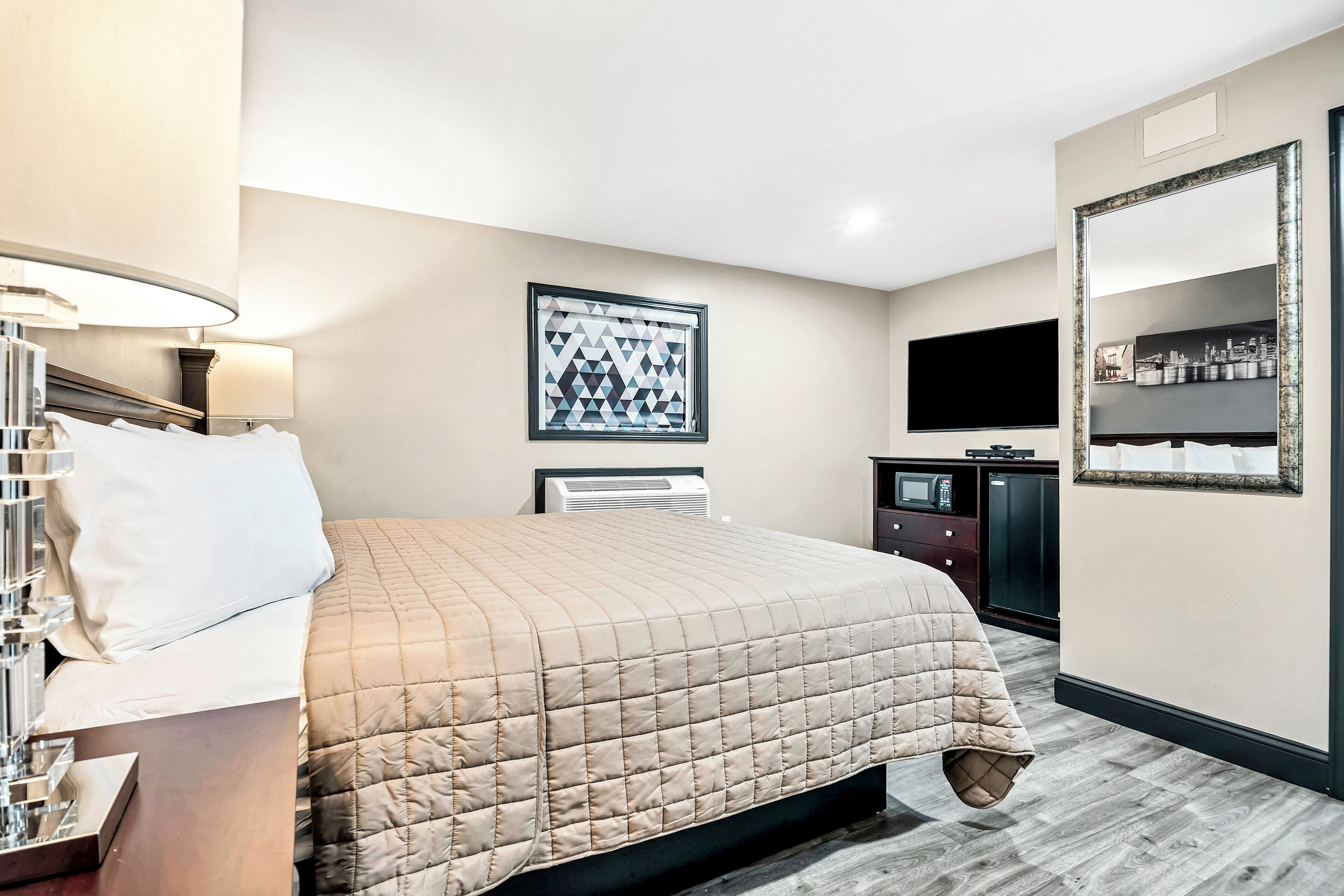 Une chambre d’hôtel équipée d’un lit, d’une télévision, d’un miroir et d’un climatiseur fixé au mur.