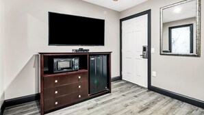 Een kamer met een flatscreen televisie aan de muur, een magnetron en een koelkast in een houten kast.