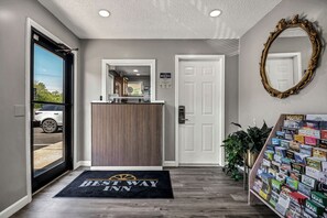 A hotel entrance with a reception desk, a black doormat, a white door, and a bulletin board with various pamphlets. - Best Way Inn (Rockfall)