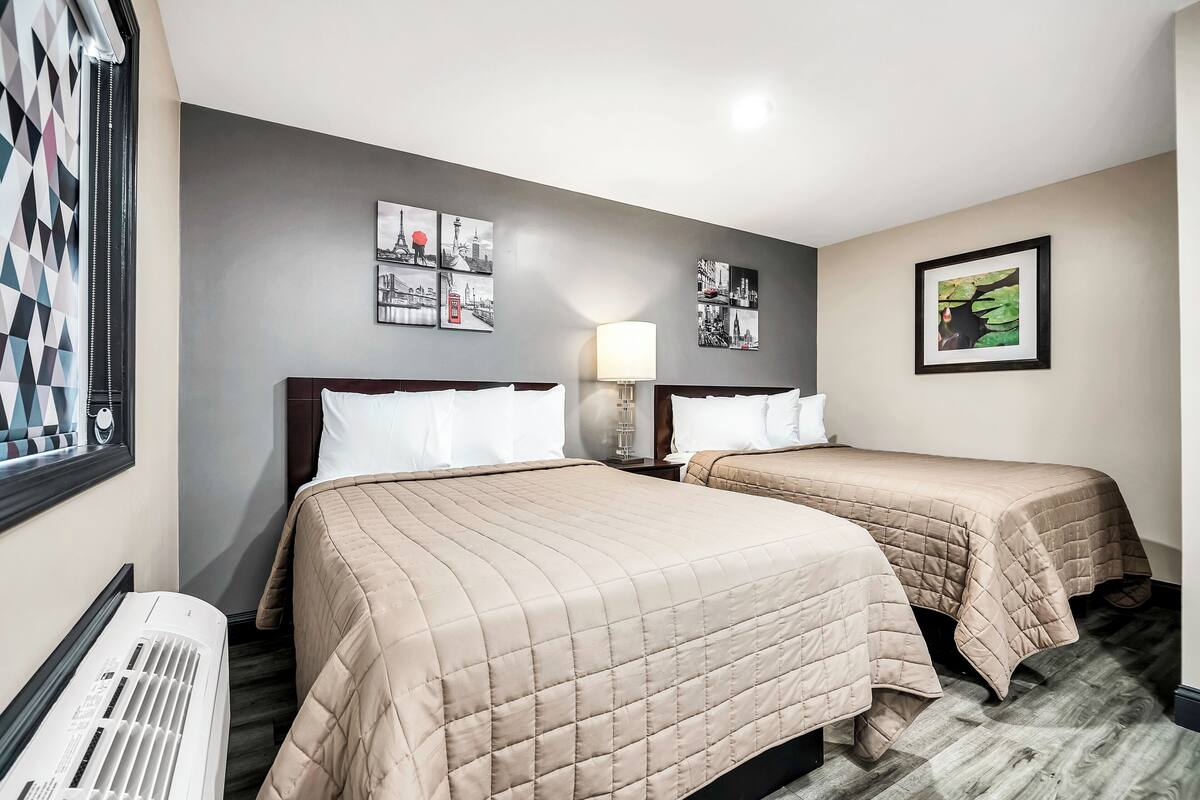 A hotel room with two beds, a wall-mounted air conditioner, and framed cityscape pictures.