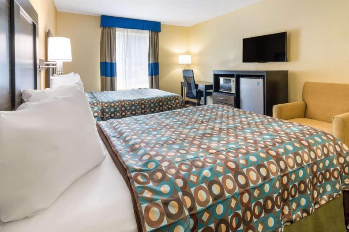 A hotel room with two beds, a desk, a chair, a television, and a microwave.