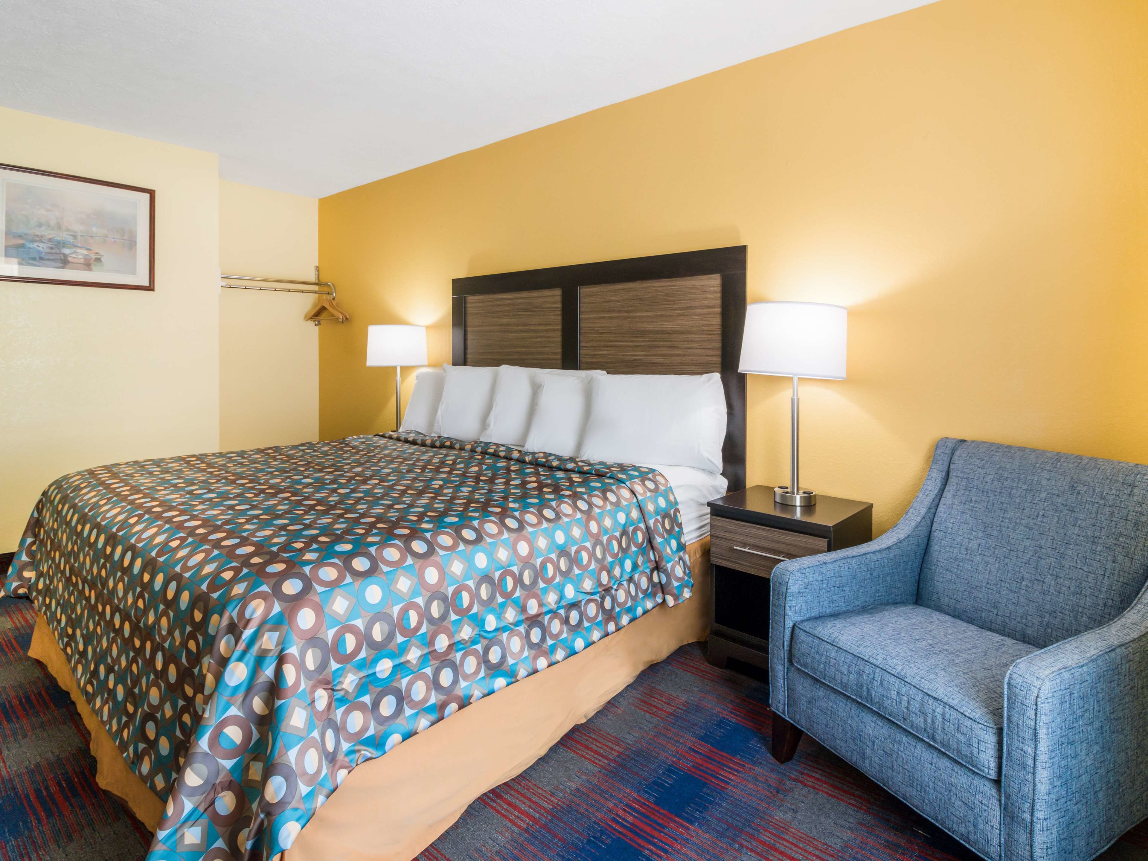 Een hotelkamer met een bed, een stoel, een nachtkastje en een lamp.