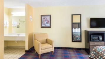 Habitación de hotel con cama, una silla, televisión, baño con lavamanos y espejo, y un cuadro en la pared.
