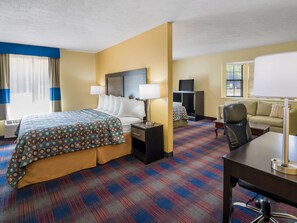 A hotel room with a bed, bedside tables, a desk, a chair, a TV, and a sofa.