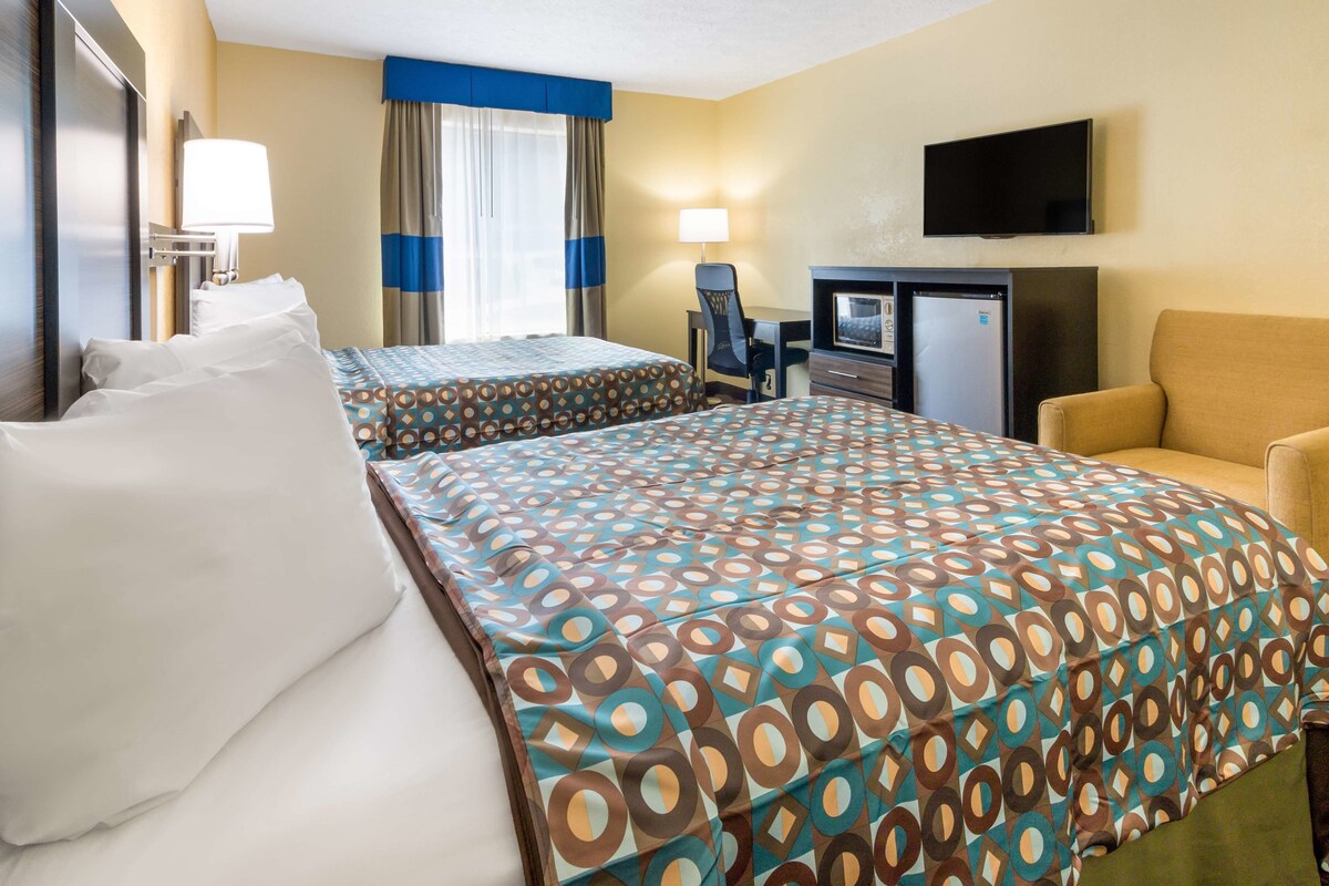 A hotel room with two beds, a desk, a TV, and a chair.