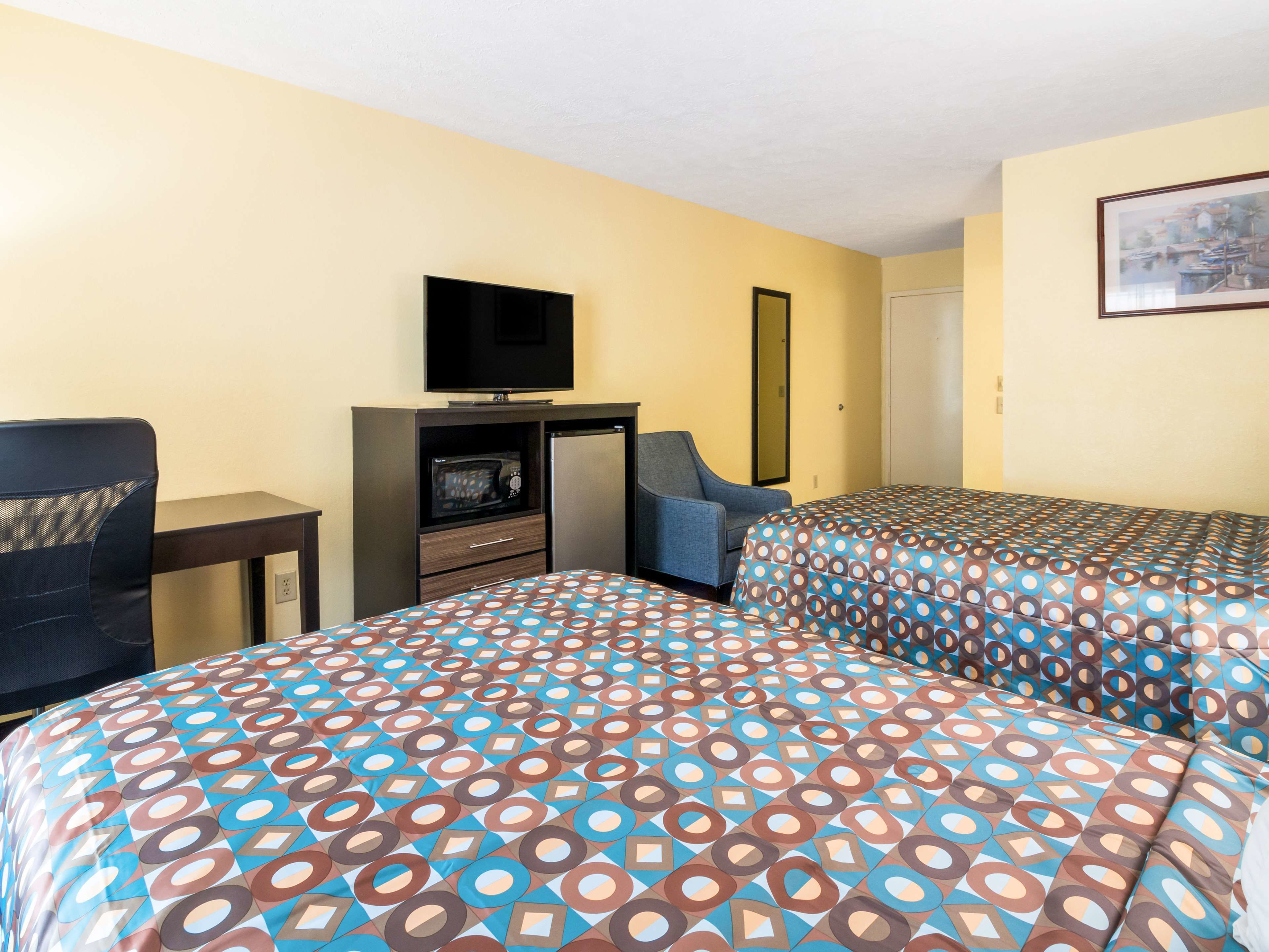 A hotel room with two beds, a desk with a television, a chair, and a door.