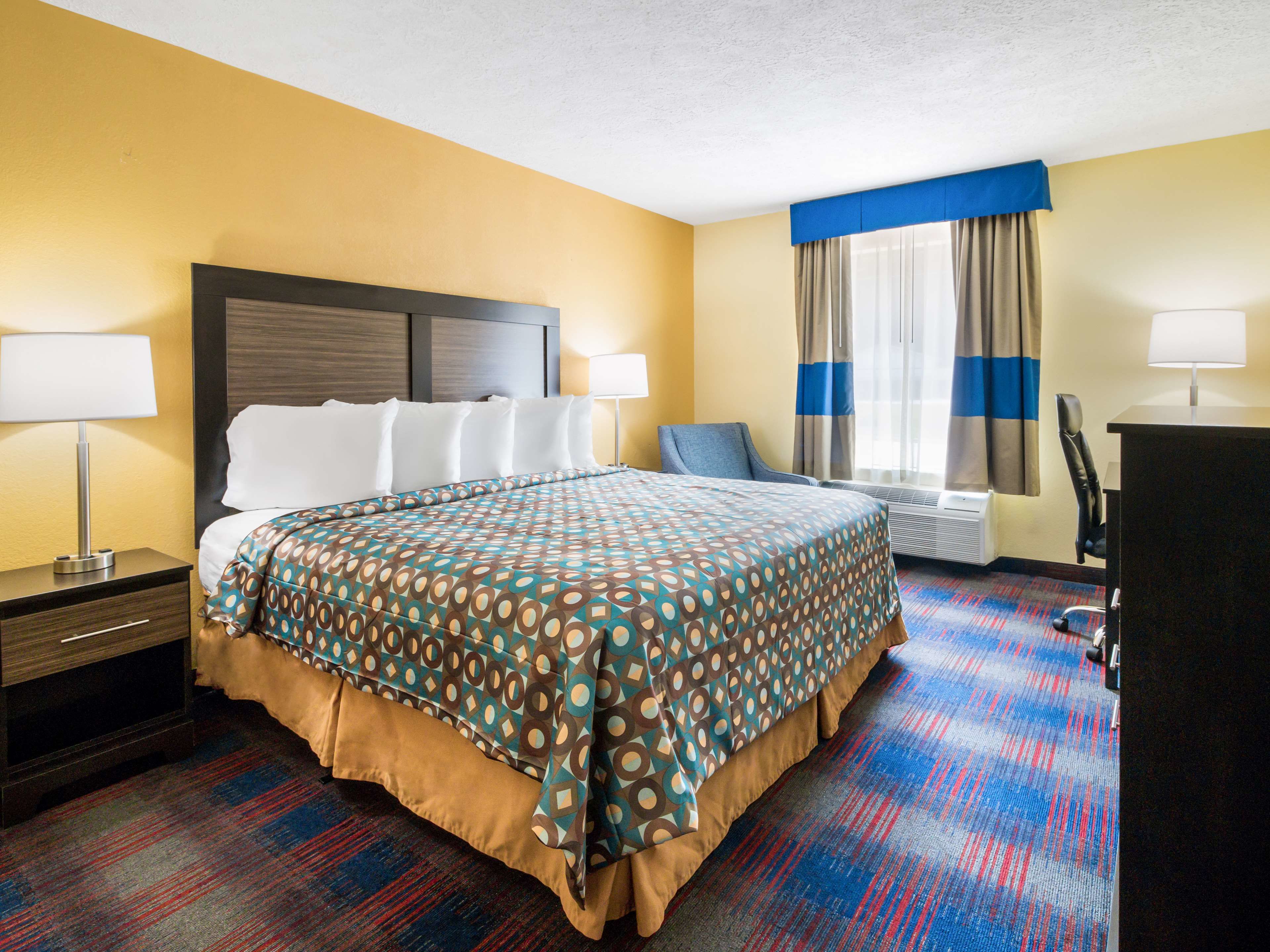 A hotel room with a large bed, two bedside tables with lamps, a desk, and a chair.