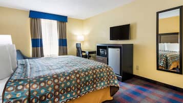 A hotel room with a bed, a desk with a computer, a TV, and a refrigerator.