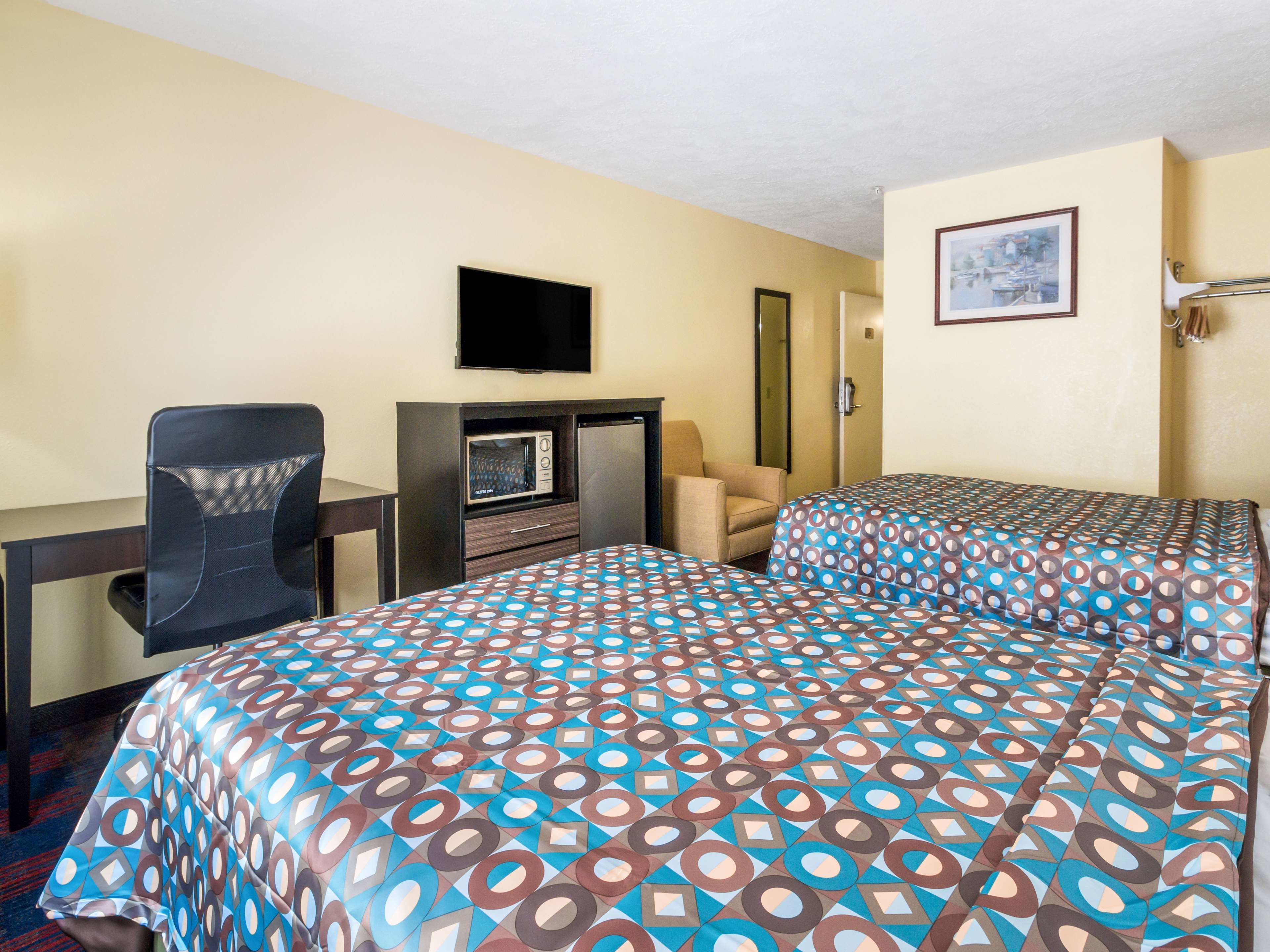 A hotel room with a bed, a desk, a chair, a television, and a microwave.