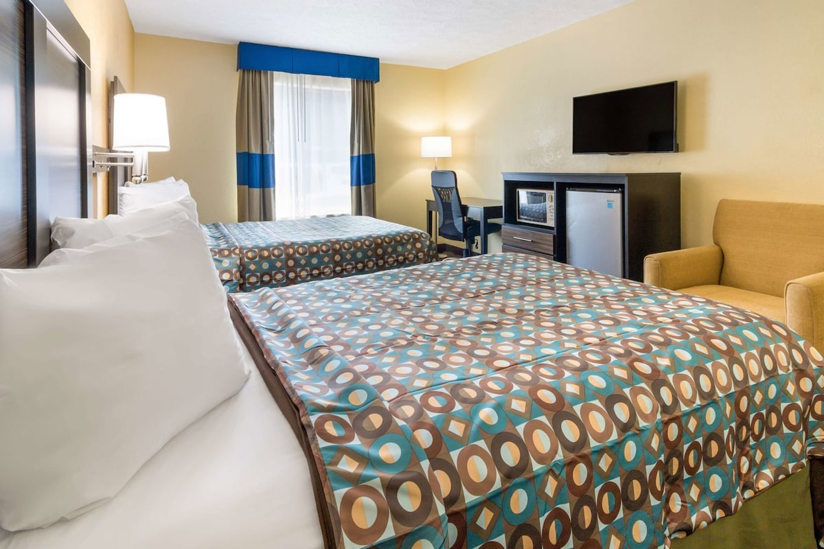 A hotel room with two beds, a desk with a computer, a TV, and a chair.
