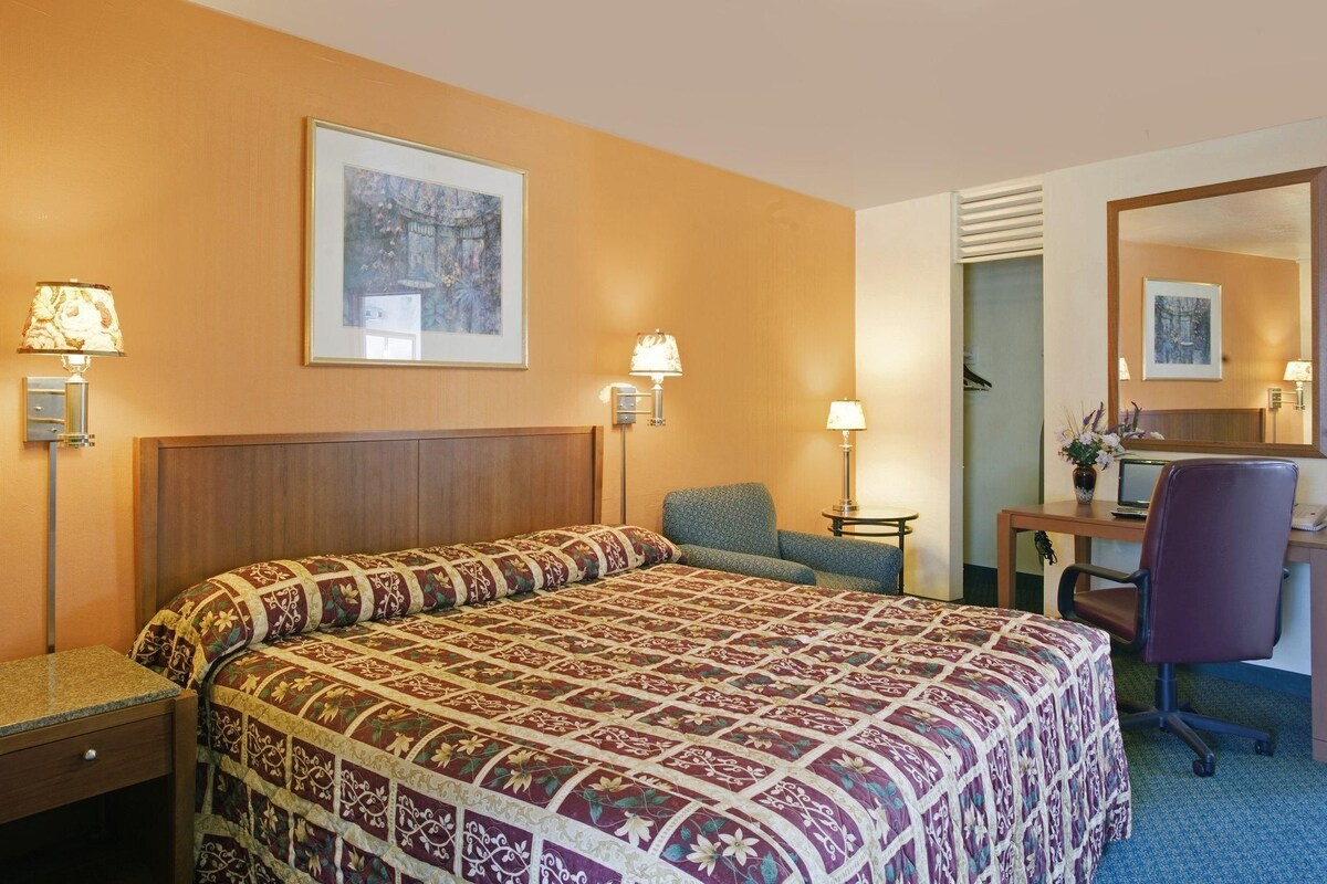 A hotel room with a large bed, a desk, a chair, and a mirror.