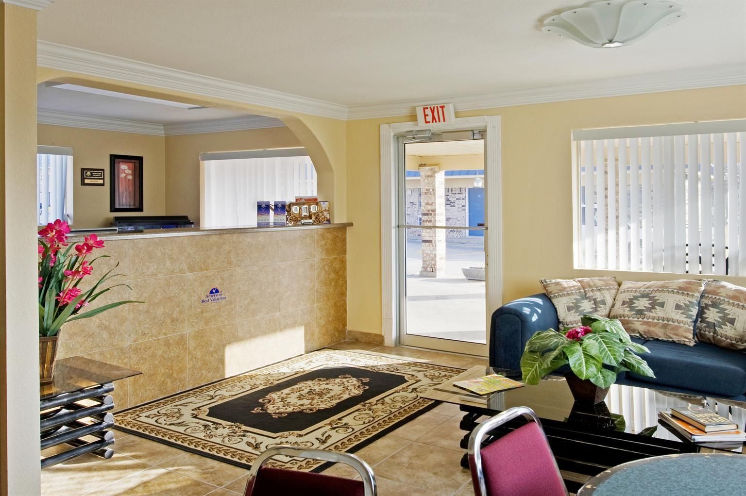 A hotel lobby with a reception desk, a blue sofa, a patterned rug, and a potted plant.