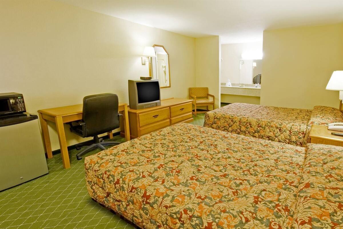 Quarto de hotel com duas camas, uma escrivaninha com computador, televisão e frigorífico.