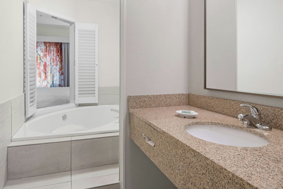 A modern bathroom with a freestanding bathtub, a granite countertop sink, and a large mirror.