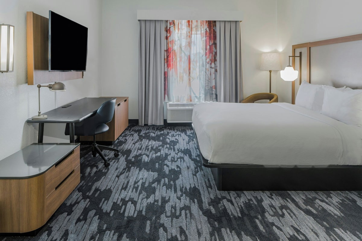 A hotel room with a bed, desk, chair, TV, and a window with curtains.