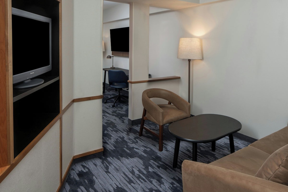 A hotel room with a flat-screen TV, a sofa, a small table, a lamp, and a desk with a chair.